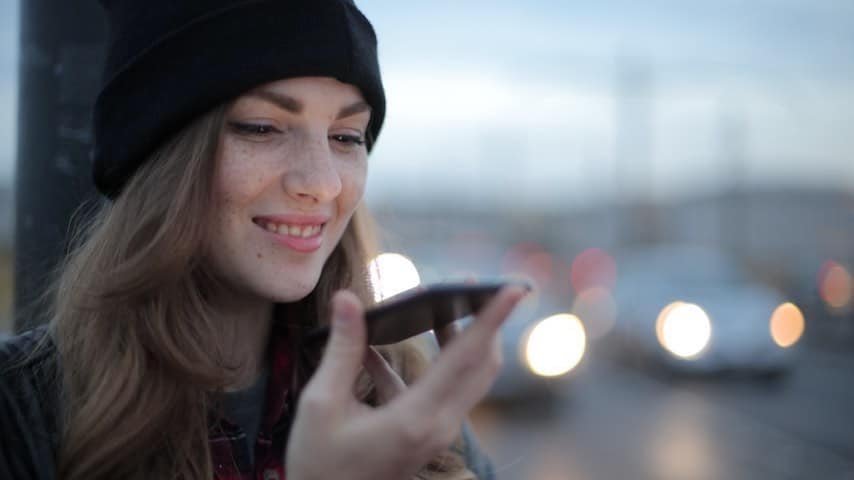 Picture illustrating a woman speaking into her phone. Retrieved from Unspalsh. For blog post “The Impact of AI on the Voice-Over Industry. https://www.pexels.com/photo/joyful-young-woman-phoning-on-street-in-evening-3776659/
