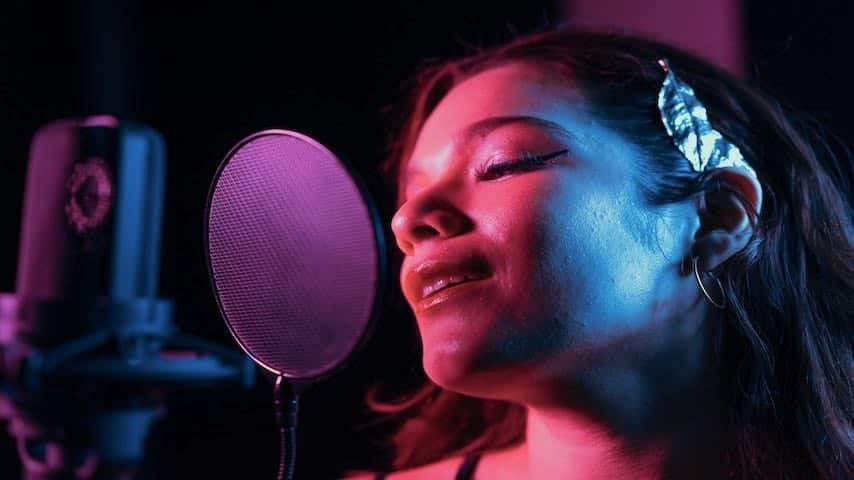 Pop Filters: The Essential Tool for Better Voice Recording. Picture of a young woman In front of a microphone with a pop filter. Picture by https://www.pexels.com/photo/close-up-shot-of-a-singer-7586648/