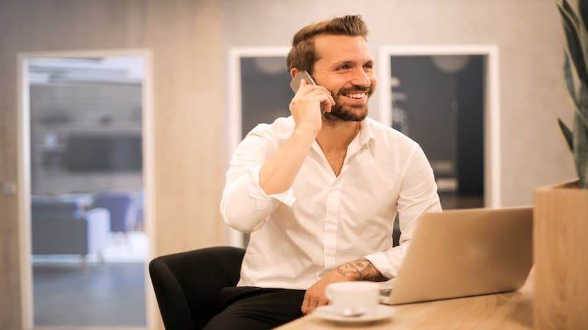 Professional voicemail greeting - Importance of a Professional Voicemail Greeting for Business. Image of a male with a white shirt and formal clothes chatting on a telephone. Image licence by Pexels: https://www.pexels.com/photo/smiling-formal-male-with-laptop-chatting-via-phone-3760263/