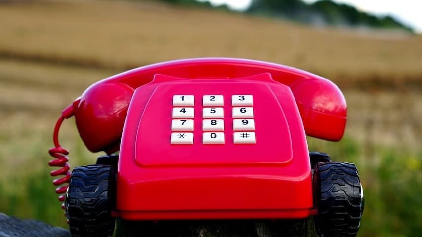 IVR Voice Over Jobs. Image of a red rotary phone with black wheels near brown grasses during day time. This image is used to illustrate the article "IVR Voice Over Jobs: Telephony Reinvented." Pexels license: https://www.pexels.com/photo/red-rotary-phone-with-black-wheels-near-brown-grasses-during-day-time-128663/