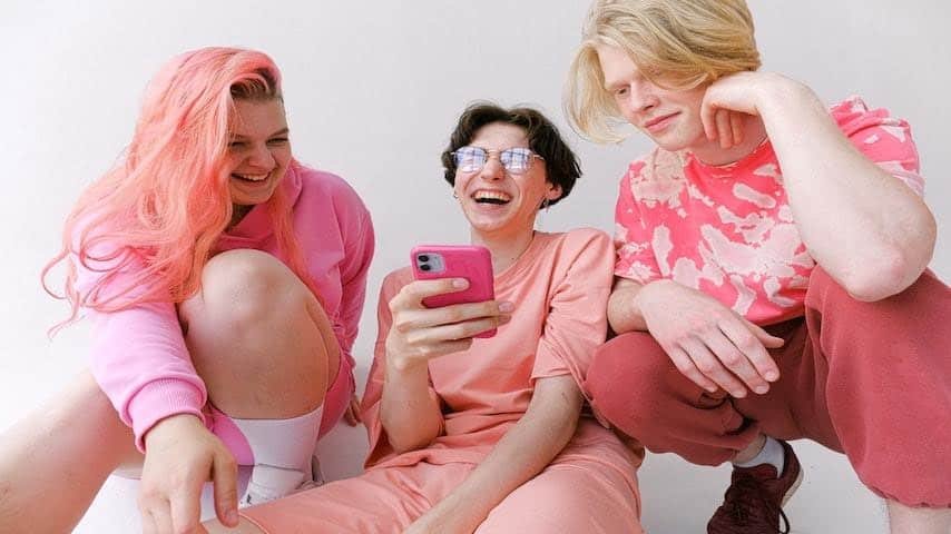 Voice Over in TikTok. Image of friends in pink clothes looking at a smartphone. This image is used to illustrate the article "How to Do Voice Over in TikTok: A Complete Guide". Pexels license: https://www.pexels.com/photo/friends-in-pink-clothes-5325597/